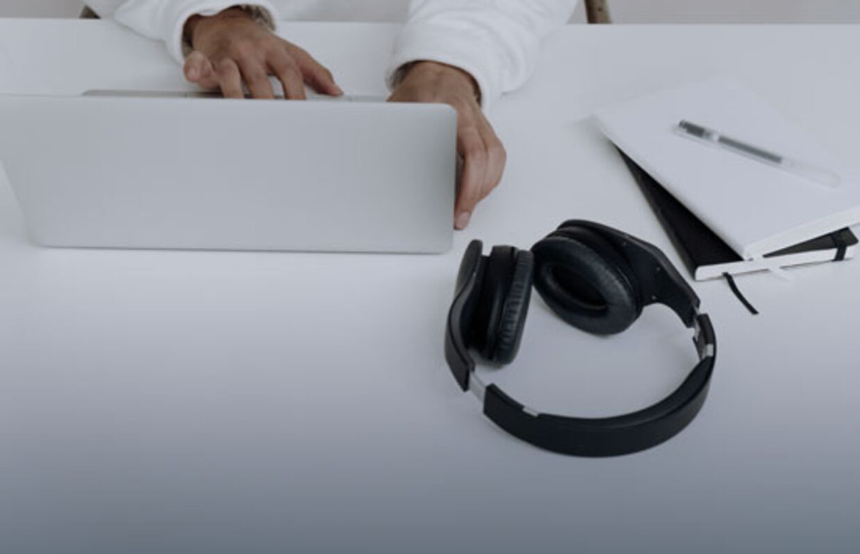 White desk with laptop, notebook and black headphones